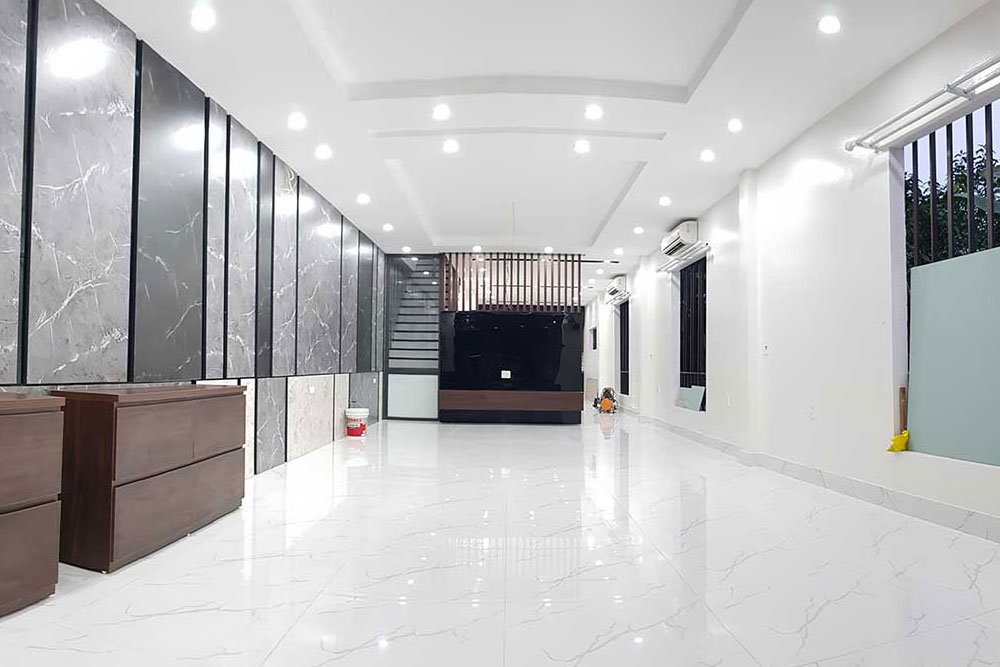 A newly renovated, modern room with polished white marble floors, sleek dark panel walls, and bright recessed ceiling lights.