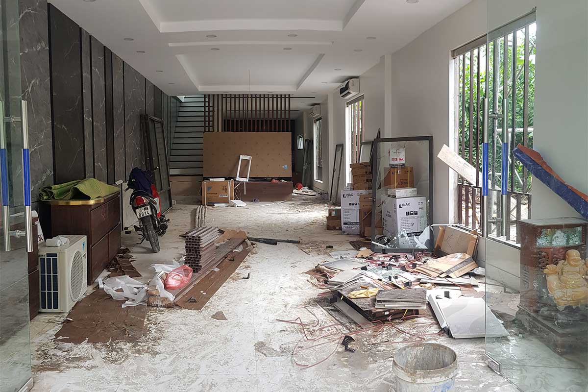 A room under renovation with scattered materials, tools, and appliances. The floor is partially covered in dust and debris.