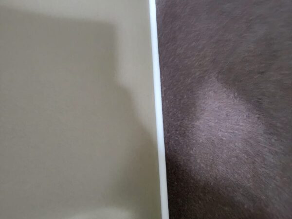 A close-up view of two surfaces meeting at a corner, one side covered in beige material and the other in a brown textured material, separated by a white trim.